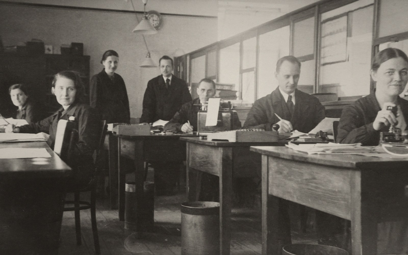 Period interior of a central European insurance office, high ceilings, wooden desks in rows, clerks at work, natural light from tall windows